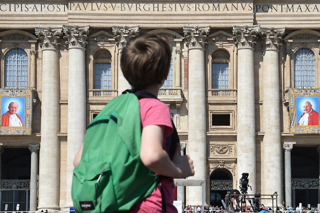 A boy looks towards the tapestries showing portraits of late Popes John Paul II (left) and John XXIII hanged on the balconies of St Peter's basilica in Vatican, two days before the two popes canonisation. Photo: AFP