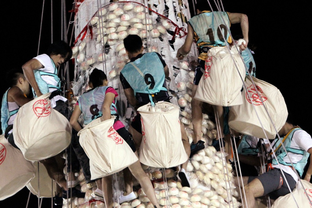 Competitors harnessed to the 40-metre tower load up with buns during the annual competition at Cheung Chau Island at midnight last night. Photo: Felix Wong