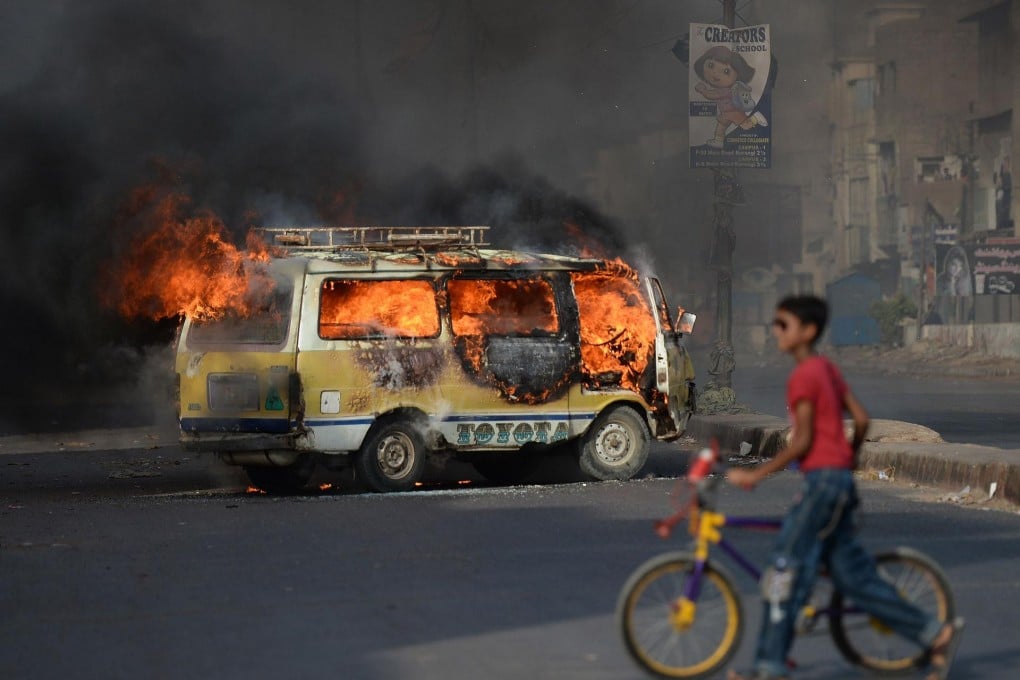 A Pakistani youth wheels his bicycle past a burning vehicle on a Karachi street following Altaf Hussain's arrest. Photo: AFP