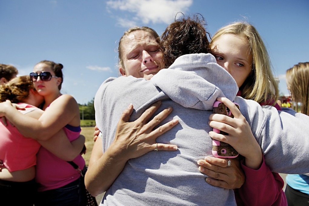 Brandi Wilson (left) and her daughter, Trisha Wilson, embrace Trish Hall, a mother waiting for her student, as students arrived at the Fred Meyer grocery store parking lot after a shooting at Reynolds High School. Photo: AP