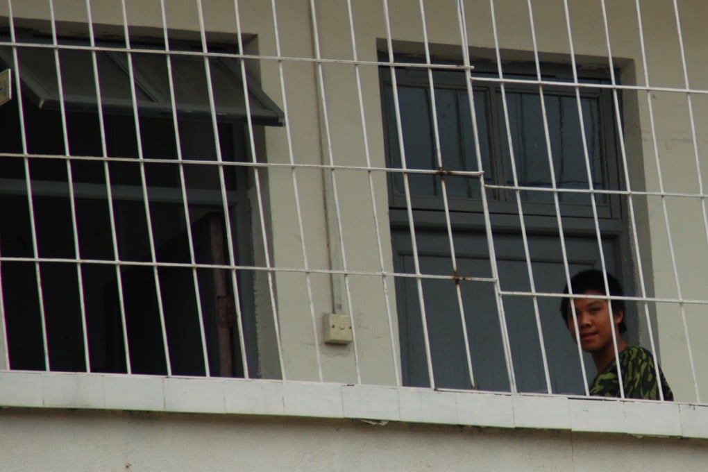 A student dressed in a military-style shirt looks out from a wire fence at a military-style boot camp. Photo: Ivan Zhai