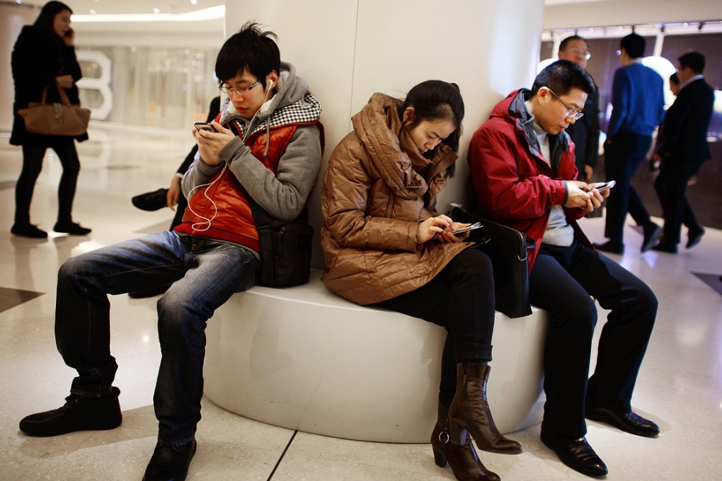 People use their mobile phones as they sit inside a shopping mall in Beijing. Photo: AFP