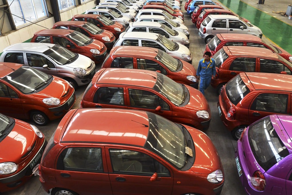 A worker walks among electric cars in a factory in Shandong province. The country wants half a million electric cars on the road by 2015, but it is still far from reaching its target. Photo: AP
