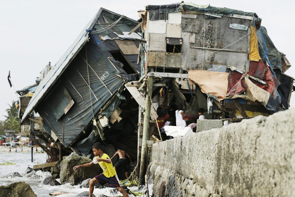A Filipino teen walks past a damaged house after strong winds and rain brought by Typhoon Rammasun in Manila. Photo: EPA