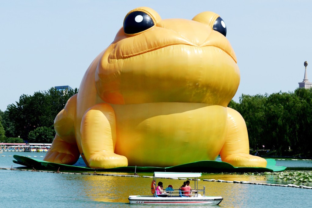 People ride in a boat before the 22-metre tall inflatable toad displayed at Yuyuantan park in Beijing. Photo: AFP