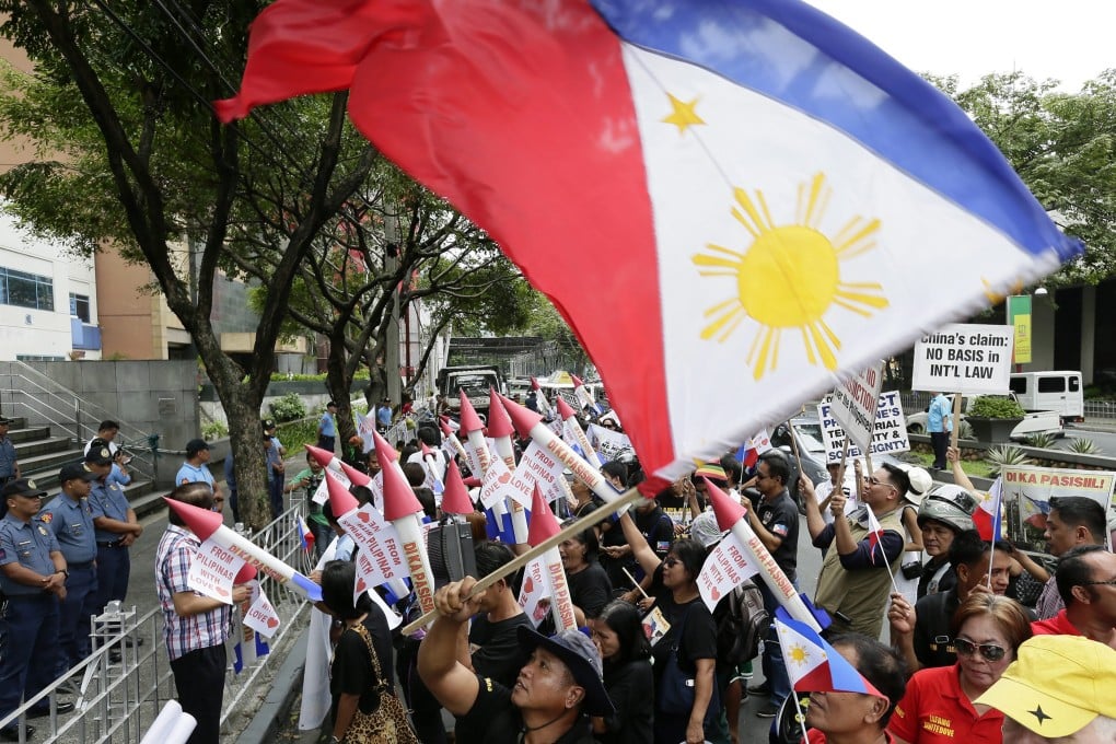A Filipino activist waves a national flag while women brandish mock missiles as they shout anti-China slogans as part of a protest against Chinese aggression in Manila's financial district on Thursday. Photo: EPA