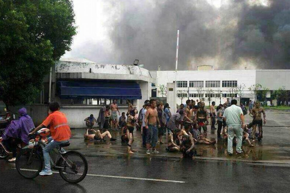 Smoke rises from the factory as workers gather outside in charred, tattered clothes following the explosion yesterday. Photo: Imagine China
