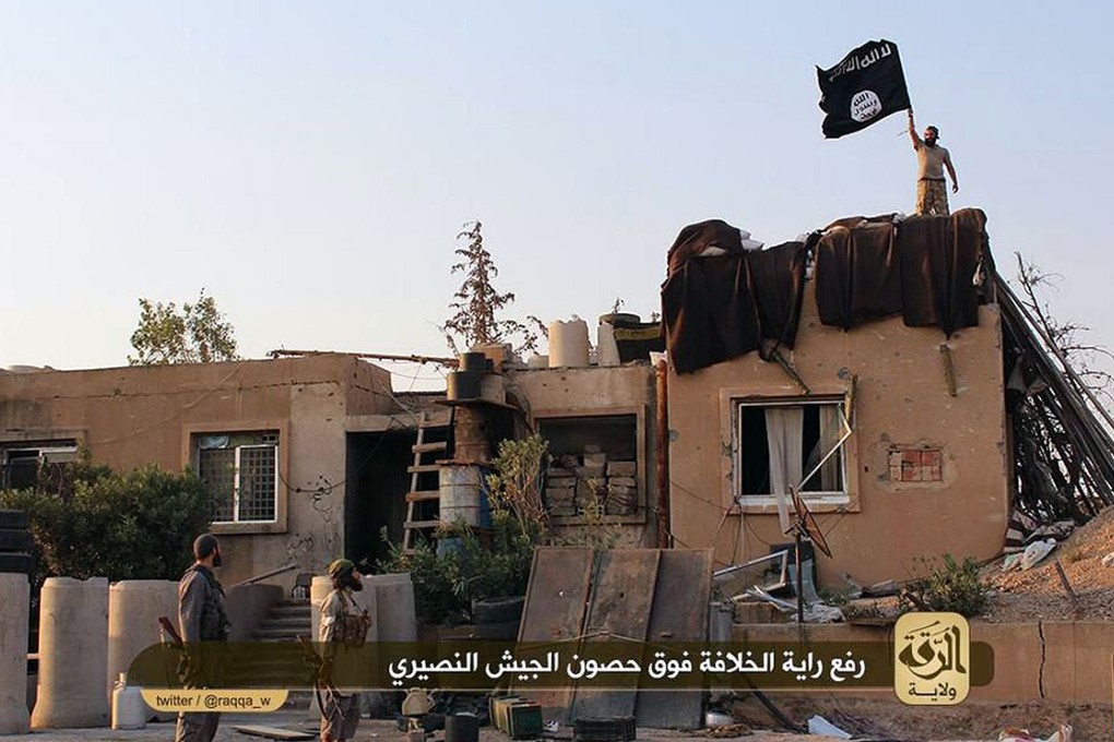 Islamic state militants raise their black and white flag over a building belonging to a Syrian army base in the northern rebel-held Syrian city of Raqa. Photo: AFP