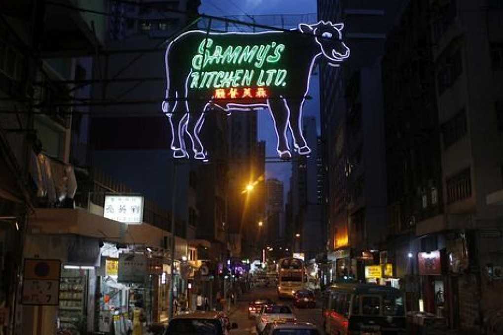 The giant neon cow sign of Sammy's Kitchen stretches across the road in Sai Ying Pun.