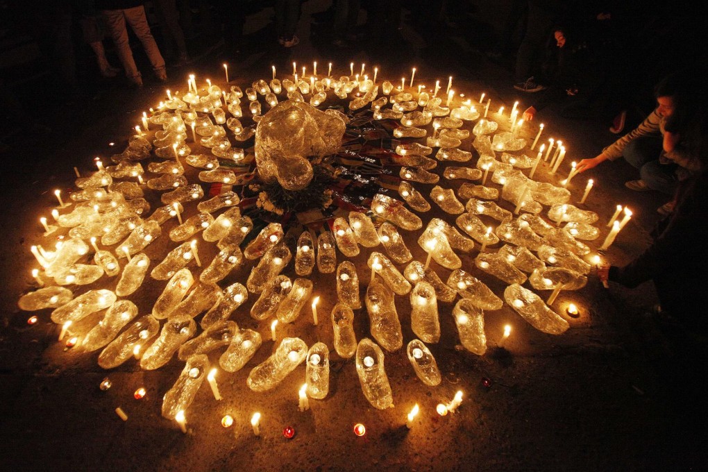 A woman lights a candle in a sculpture of acrylic shoes and a person representing the victims of 1973 military coup on Thursday. Photo: AP