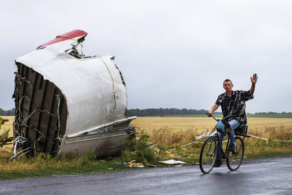 A man gestures as he rides a bicycle past a large piece of wreckage of the downed Flight MH17, near the village of Hrabove on Tuesday. Photo: Reuters
