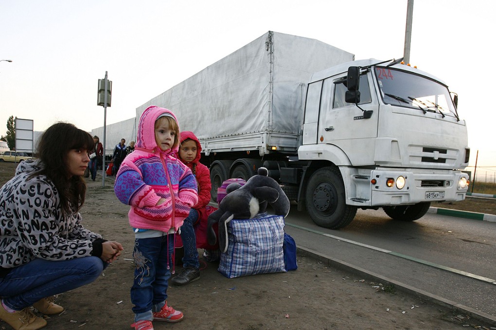 Lorries, part of a Russian humanitarian convoy, cross the Ukrainian border at the Donets'k-Izvarino checkpoint early on Saturday as Ukrainian refugees look on. Photo: AFP