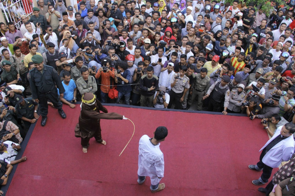 An sharia law official whips a man convicted of gambling with a rattan cane watched by people inside a mosque compound in Banda Aceh on Friday. Photo: AP