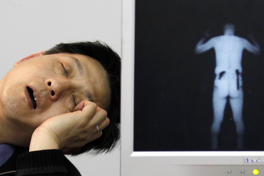 A salesman, manning an exhibit of X-ray equipment, sleeps next to an image of a man with weapons attached to his body at a China police equipment exhibition. Photo: Reuters