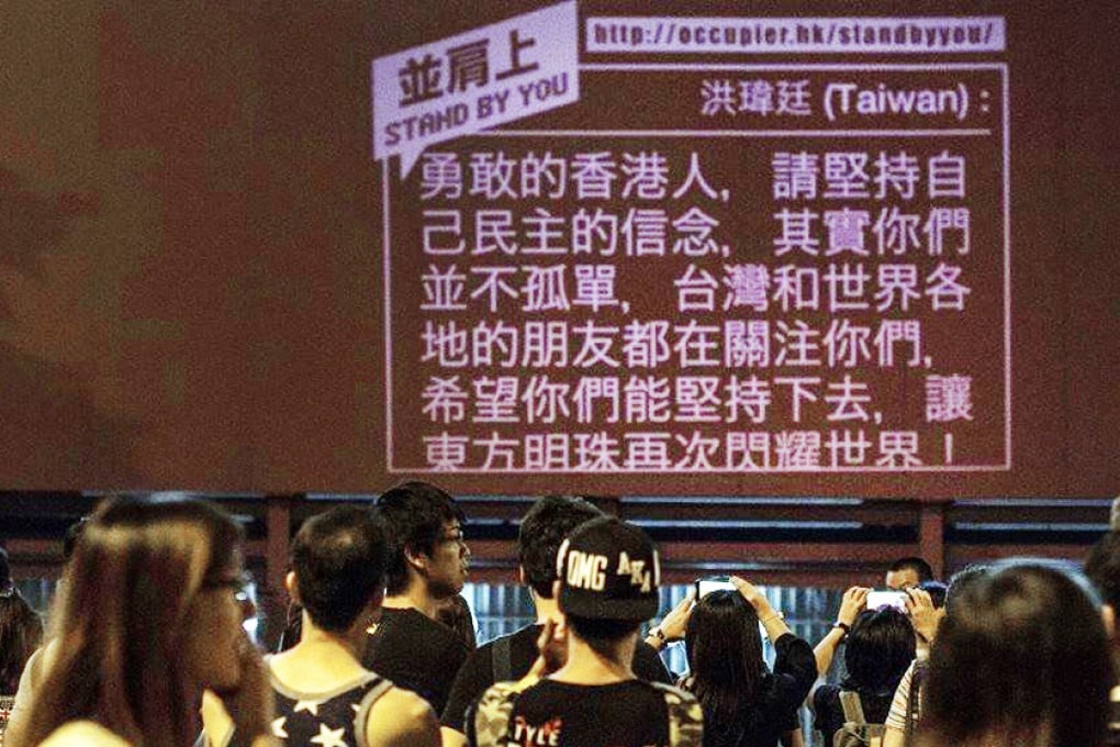 Protesters and passersby look at messages of support from around the world for Occupy Central projected next to Gloucester Road. Photo: Stand By You