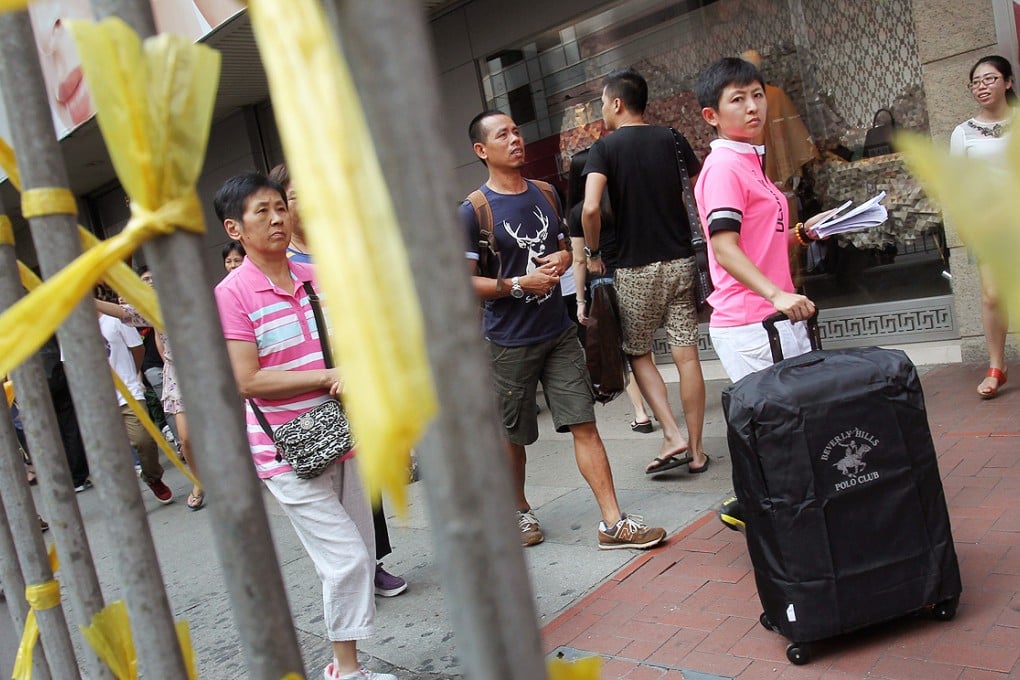 Mainland tourists pass an Occupy Central sign in Causeway Bay yesterday. Fewer mainlanders will be visiting the city after package tours were suspended. Photo: May Tse