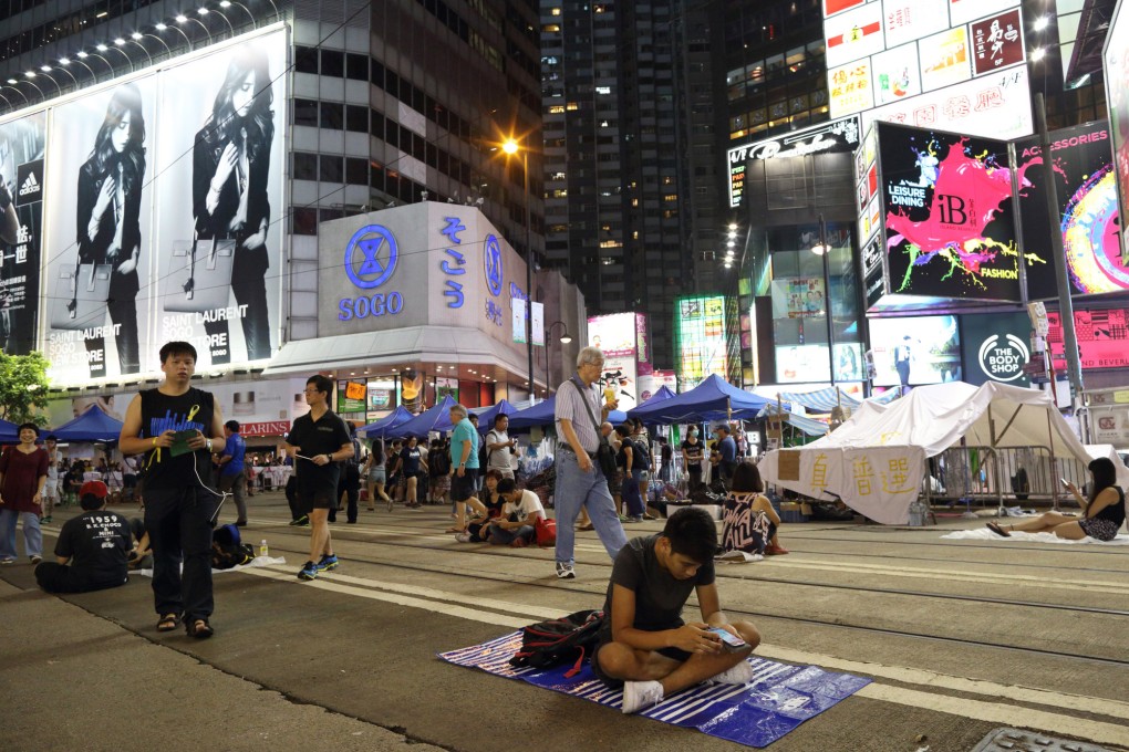 A protester sits on a road during ongoing protests as pedestrians walk past in Causeway Bay.