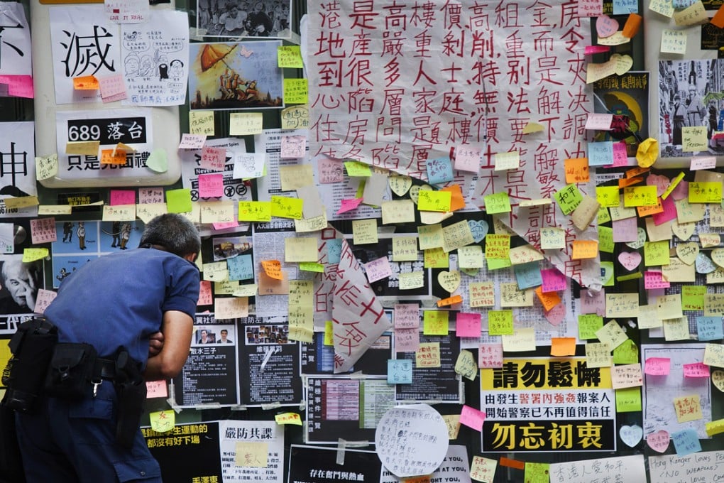 A policeman reads messages of support for the pro-democracy movement stuck on the side of HSBC bank on Friday. The artwork was removed on Wednesday. Photo: EPA