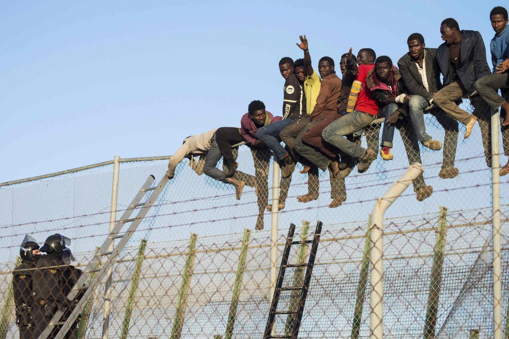 Migrants sit on a border fence, as guards look on. Photo: Reuters