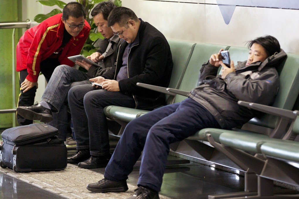 Men browse their tablet computers and smartphone at the Beijing Capital Airport in Beijing. Photo: AP