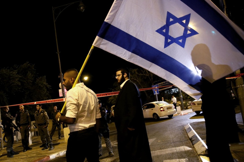 Israeli security forces stand behind a security perimeter as Israelis wave flags at the site where Yehuda Glick was shot. Photo: AFP