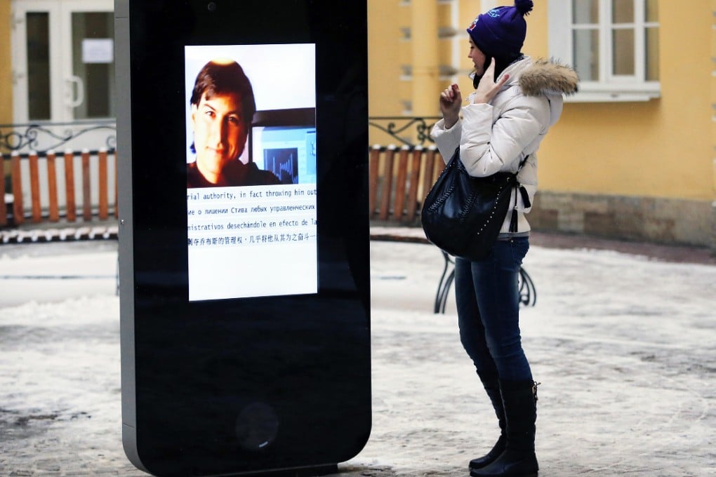 A woman stands next to a screen showing a portrait of Steve Jobs on a memorial to the late Apple founder in St Petersburg. It was removed on Friday after current Apple CEO Tim Cook came out as gay. Photo: AP
