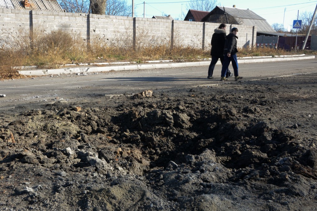 Teenagers pass by a hole in the ground from shelling in the Kuybishevskiy district, in Donetsk. Photo: AP