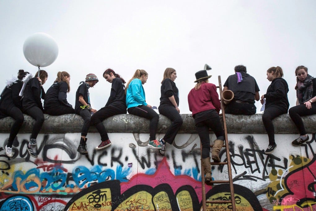 Youths sit on the East Side Gallery and watch a performance by Circus Cabuwazi and the high wire group 'Geschwister Weisheit' entitled 'Circus overcomes borders' in Berlin. Photo: EPA
