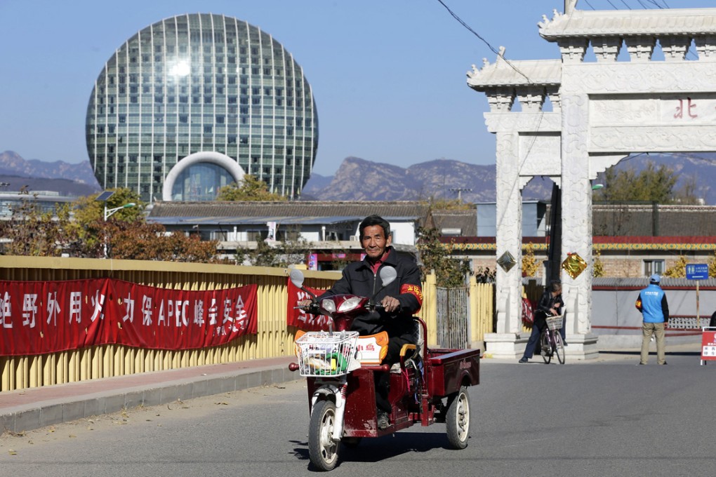 A man rides a tricycle past banners with the words "Ensure Apec summit's safety, open burning is prohibited" on display at a main road entrance to the Upper Beitai, the village closest to the venue for the meeting, in the Huairou district of Beijing. Photo: AP