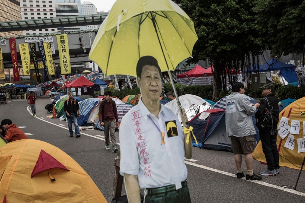 People walk past a cardboard cutout of Chinese President Xi Jinping holding an umbrella as it stands among tents outside the Central Government Offices in Admiralty.