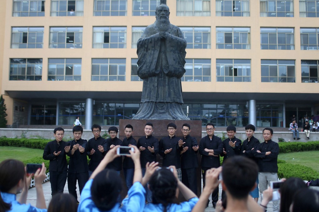 Chinese college graduates pose for their graduation photograph beside a statue of Confucius.