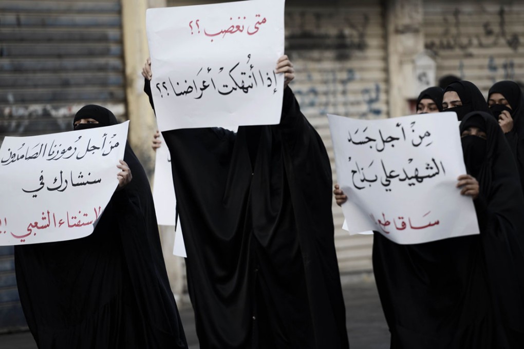 A Bahraini women (left) holds up a placard reading in Arabic "For our steadfast leaders, we will participate in the referendum", during voting in an unofficial referendum. Photo: AFP