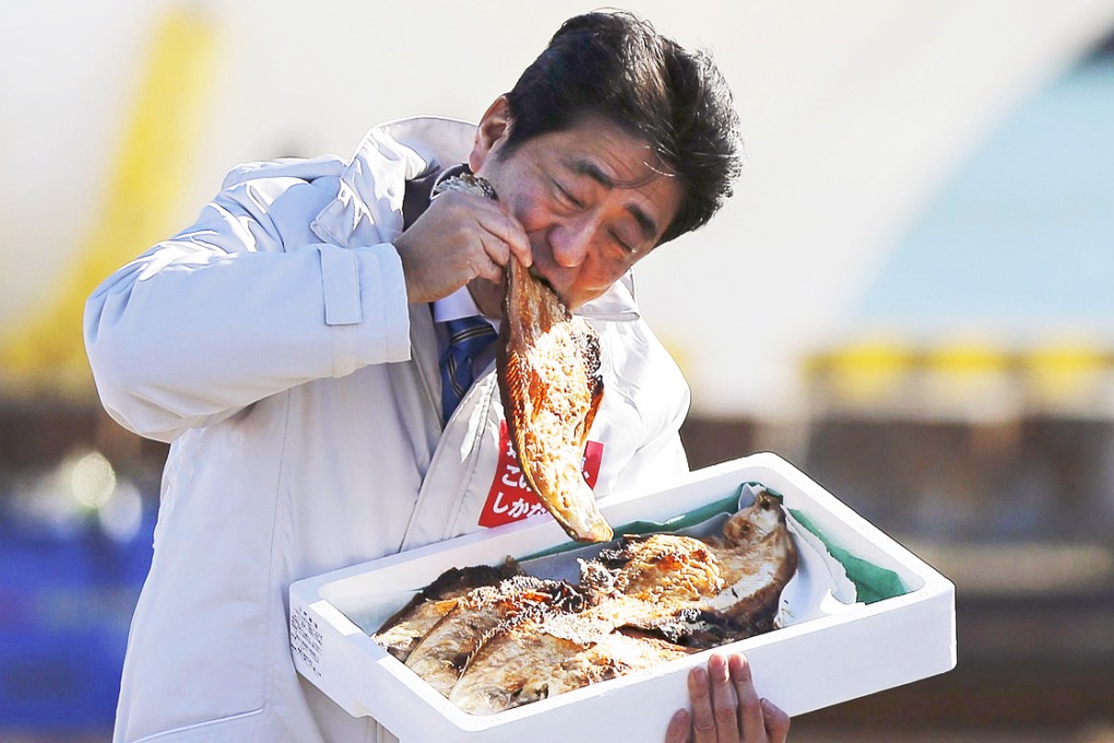 Shinzo Abe tucks into some grilled fish in the port of Soma. His Liberal Democratic Party may lose seats in the election. Photo: Reuters