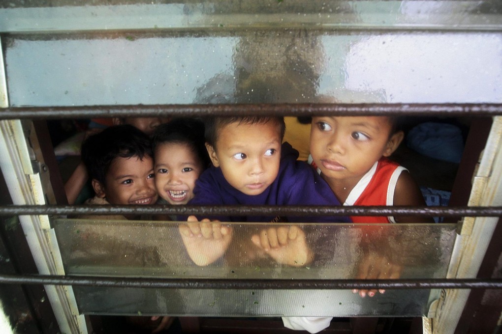 Filipino children peer out a window inside a school turned into a temporary evacuation centre in Northern Cebu province as Typhoon Hagupit knocked out power and flattened houses. Photo: EPA