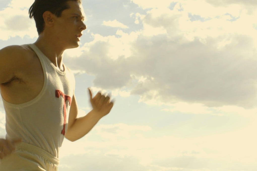 Jack O'Connell plays Louis Zamperini as an athlete and an airman adrift at sea (below) in Unbroken.