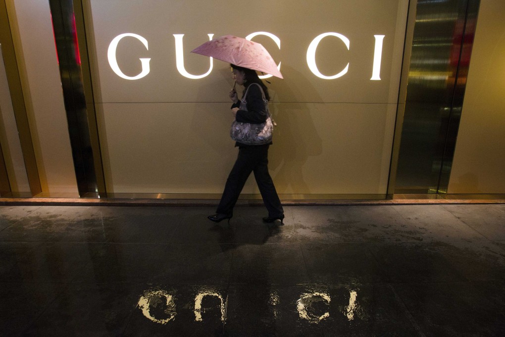 A woman holding an umbrella walks past a company logo of a Gucci boutique outside a shopping mall amid rainfall in central Guangzhou, Guangdong province February 25, 2014. Photo: Reuters
