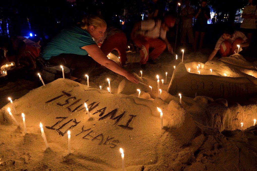 Thai students and foreign tourists place candles on a sand sculpture during commemorations on the the tenth anniversary of the 2004 tsunami at Patong beach in Phuket. Photo: AFP