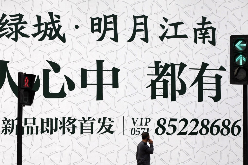 A man talks on his mobile phone as he walks past an advertising billboard outside the Greentown residential construction site in Hangzhou. Photo: Reuters