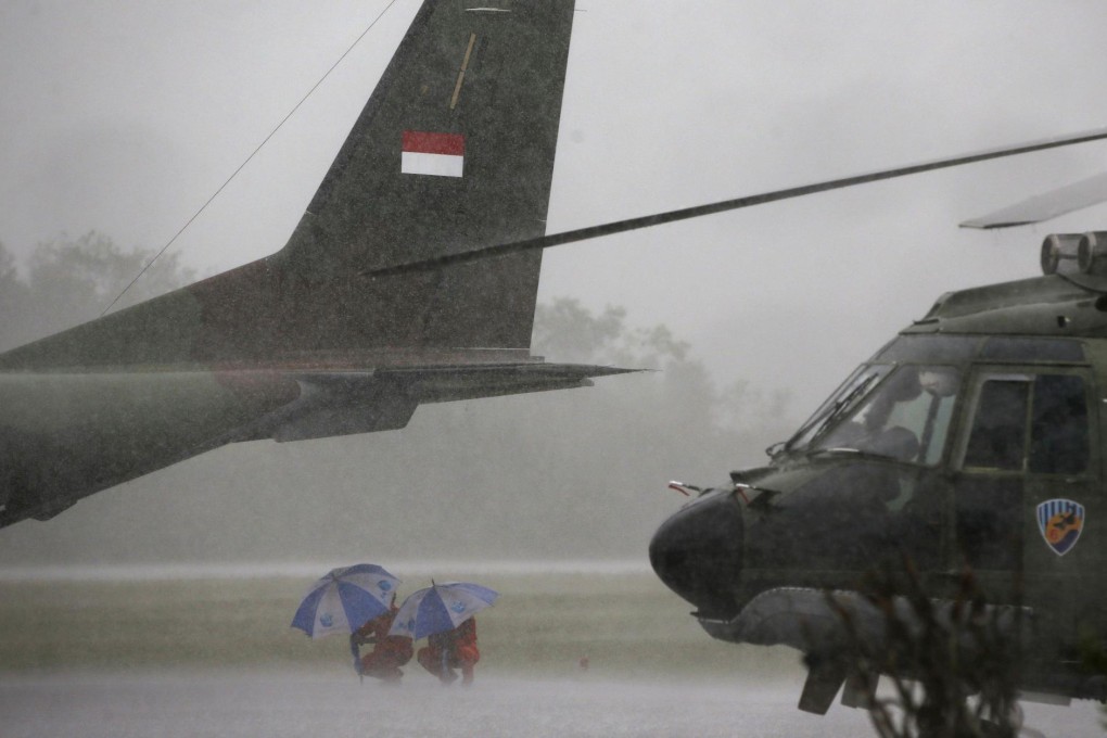 Indonesian Air Force crew members taking part in the search for the plane wait out a rain storm under a cargo plane. Photo: Reuters