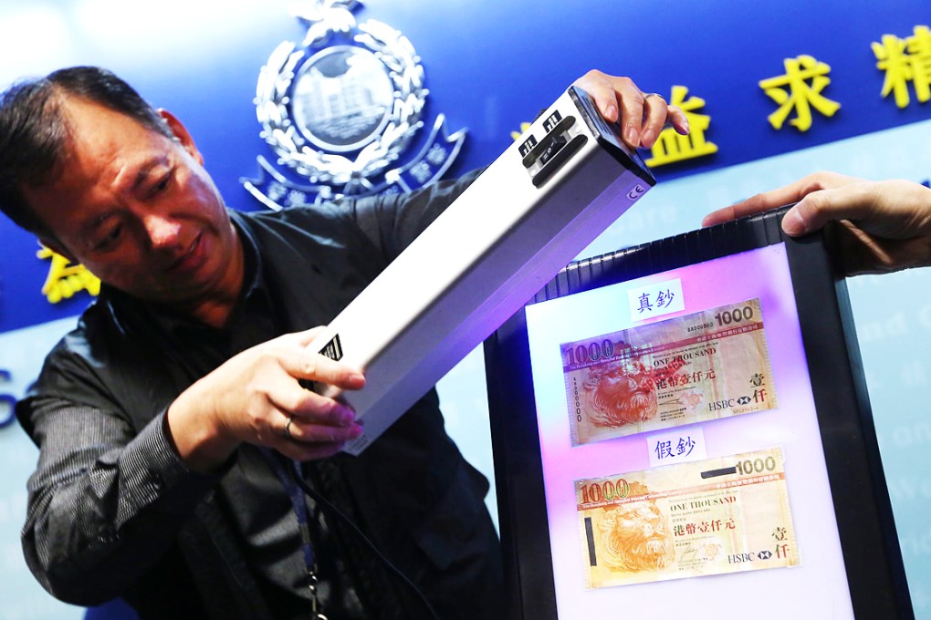 A police officer shines a light on a real and fake HK$1,000 banknote. Photo: Sam Tsang