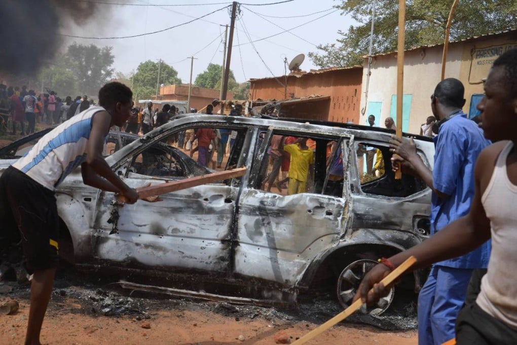 People carry sticks near damaged cars during a demonstration against Charlie Hebdo’s Mohammed cartoon in Niamey. Photo: AFP