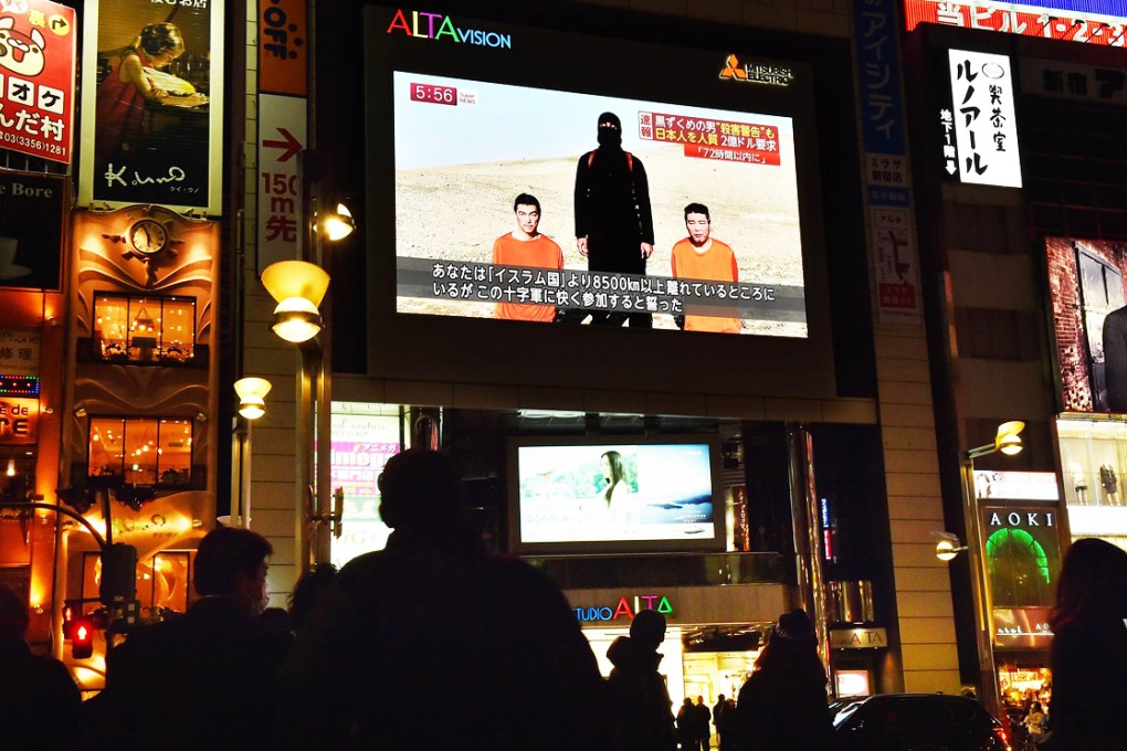 People look at a large TV screen in Tokyo on Tuesday showing news reports about the two Japanese men (in orange) who have been kidnapped by the Islamic State. Photo: AFP