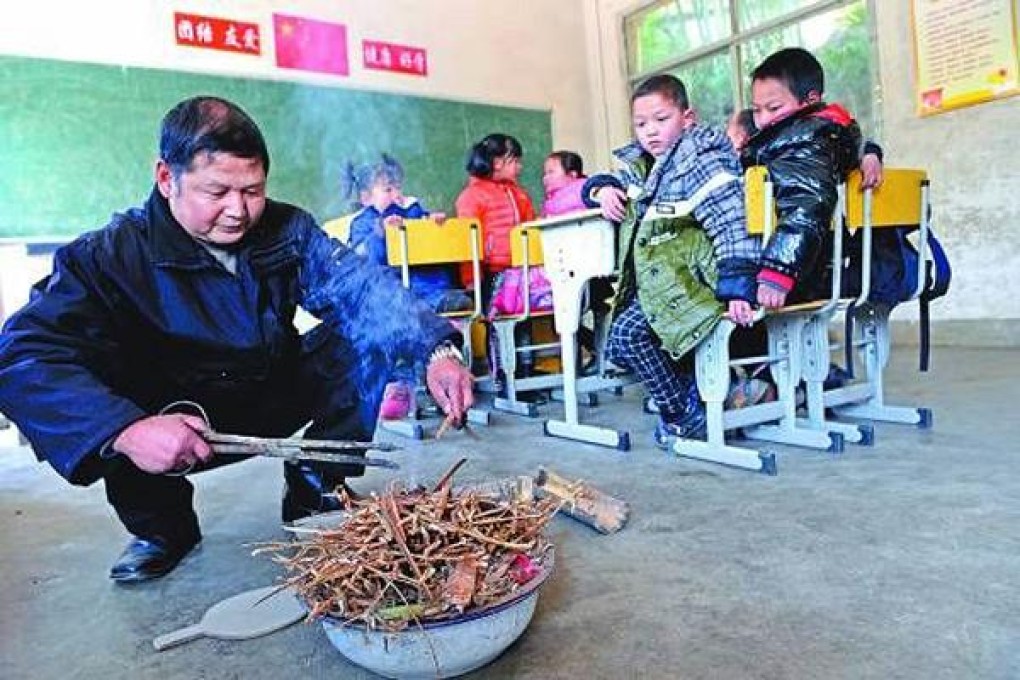 A teacher lights a fire of kindling to keep his pupils warm at their school in the mountains of Jiangxi. The local power grid is not strong enough to support electric heating at the school. Photo: SCMP