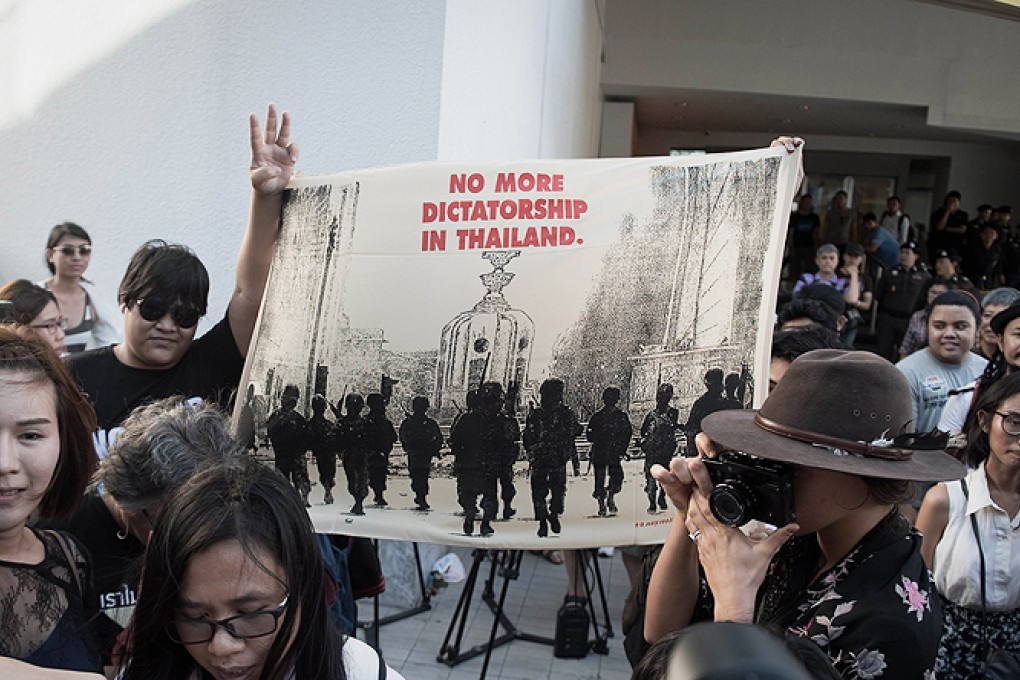 A protester makes a three-fingered salute as he holds aloft a banner calling for the return of democracy. Photo: AFP