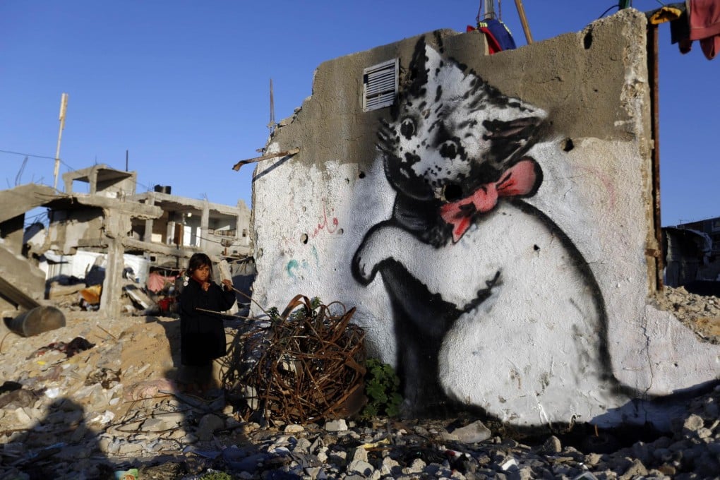 A Palestinian child next to a Banksy mural of a kitten painted on rubble from last year's war between Israel and Hamas. Photo: AFP