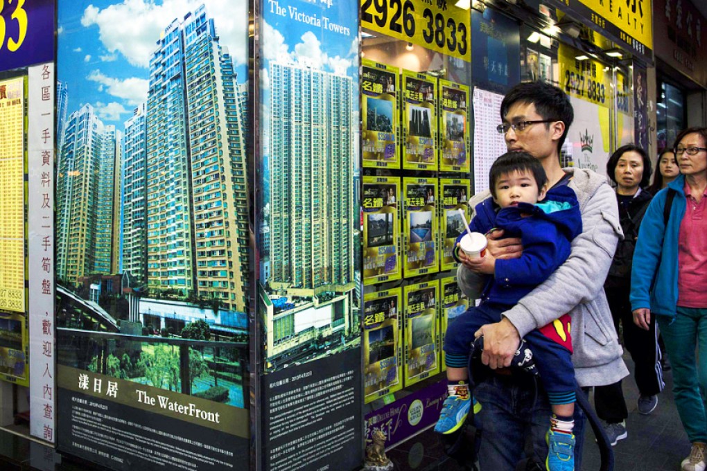 A man carrying a boy walk outside a property agency featuring posters of the latest high-rise apartment buildings. Photo: Reuters