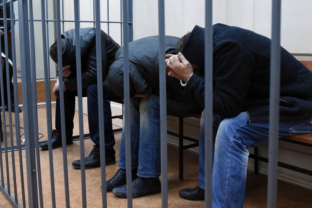 Three of the five suspects in the murder of Boris Nemtsov hide their faces inside a cage in a Moscow court yesterday. Photo: AFP