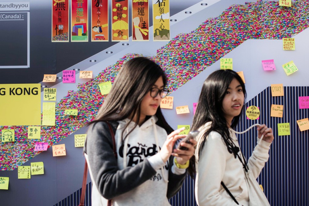 Two girls walk past a billboard depicting the "Lennon wall" during the Occupy Central movement. The city has been plagued by a culture of suspicion that divides its people into polar opposites and sometimes blinds them to common sense. Photo: AFP