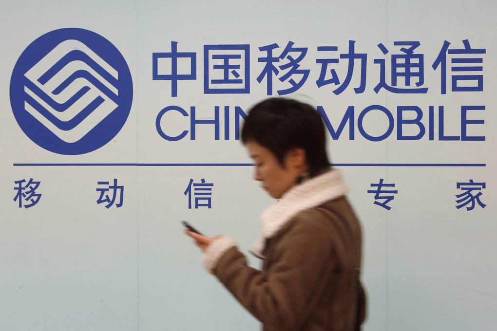 A woman looks her phone while walking past a China Mobile sign in Shanghai. The company saw a 10.2 per cent drop in profits in the fourth quarter of 2014. Photo: Reuters