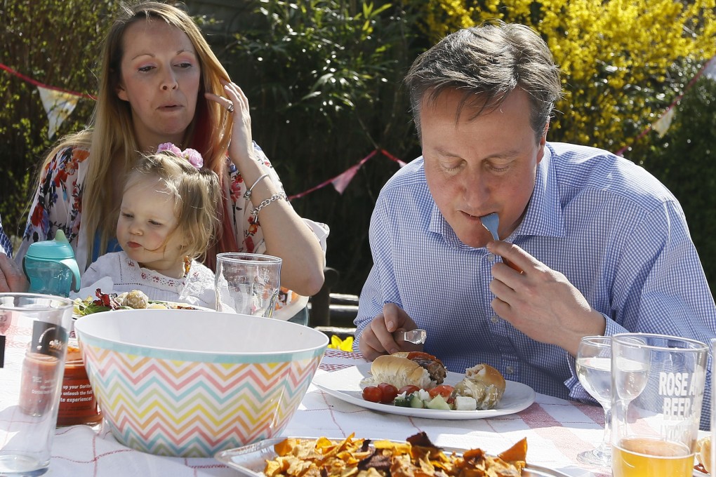 Britain's Prime Minister David Cameron enjoys his hot dog the civilised way - with a knife and fork - with Lilli Docherty and her daughter Dakota in their garden in southern England on Monday. Photo: AFP